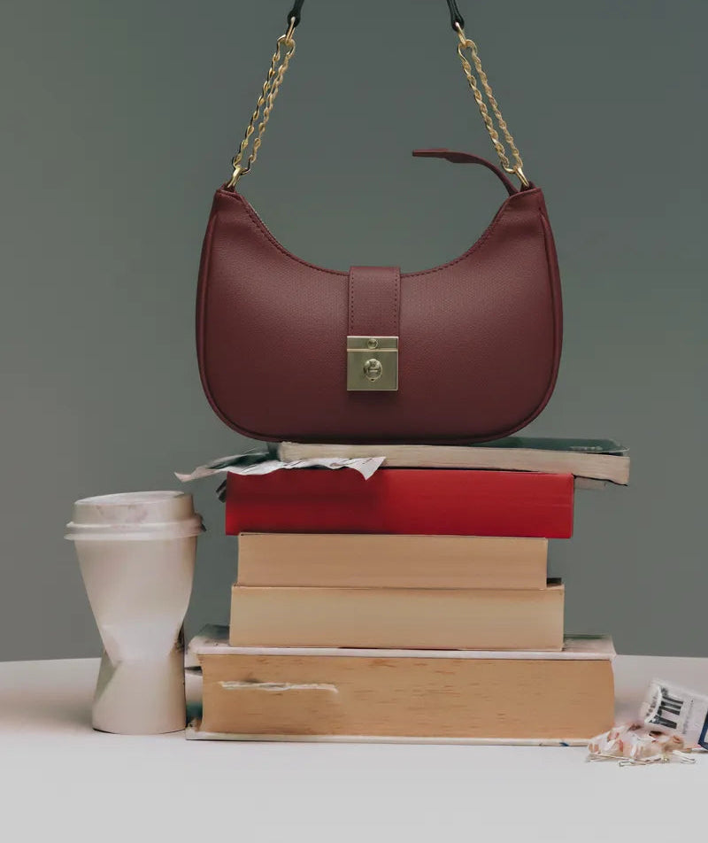 Maroon handbag on a stack of books with a gray background