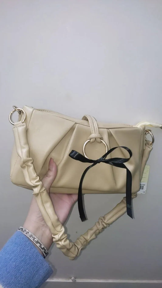 Beige handbag with a black ribbon held by a person against a plain background
