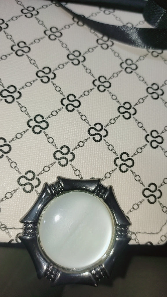 Decorative pendant with a circular white stone on a patterned fabric background