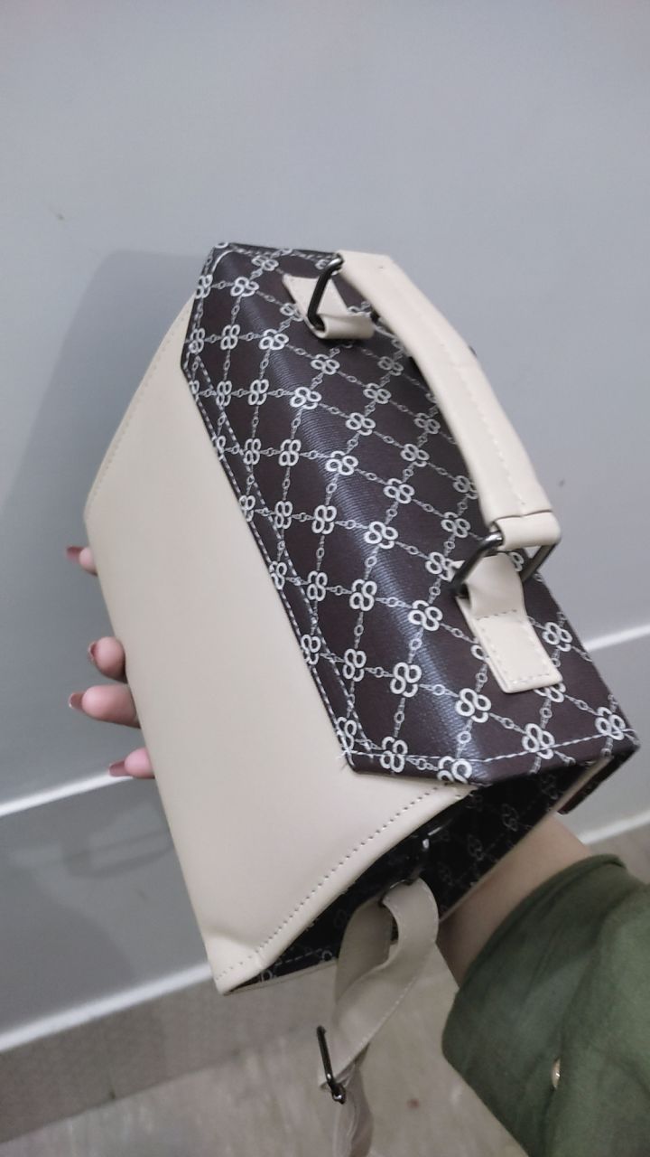 Hand holding a white bag with a black patterned flap against a light gray background