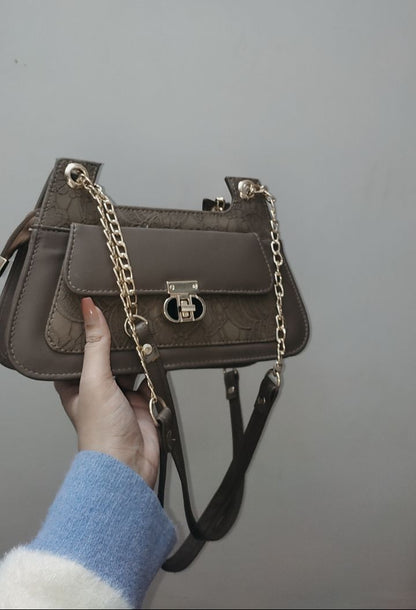 Brown handbag with a chain detail held by a person against a plain background