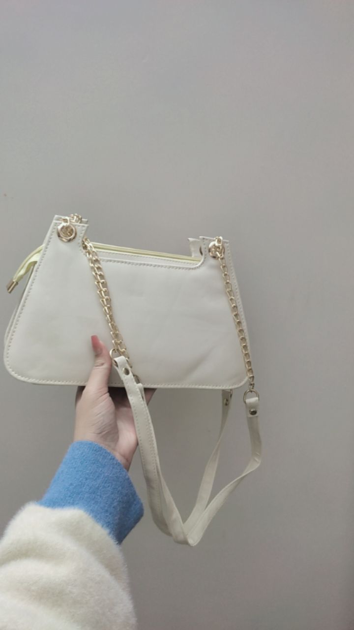 White handbag with gold chain detail held by a person against a plain background