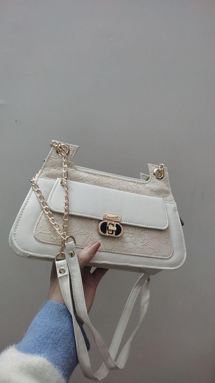 White handbag with gold accents held by a person against a gray background