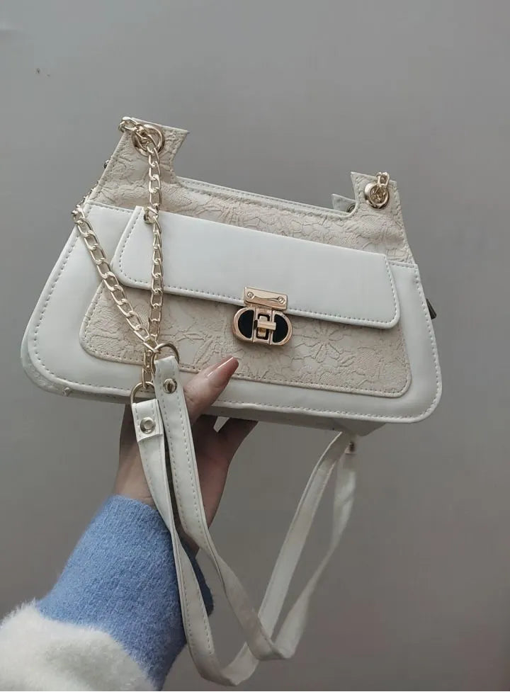White handbag with gold chain detail held by a person against a gray background