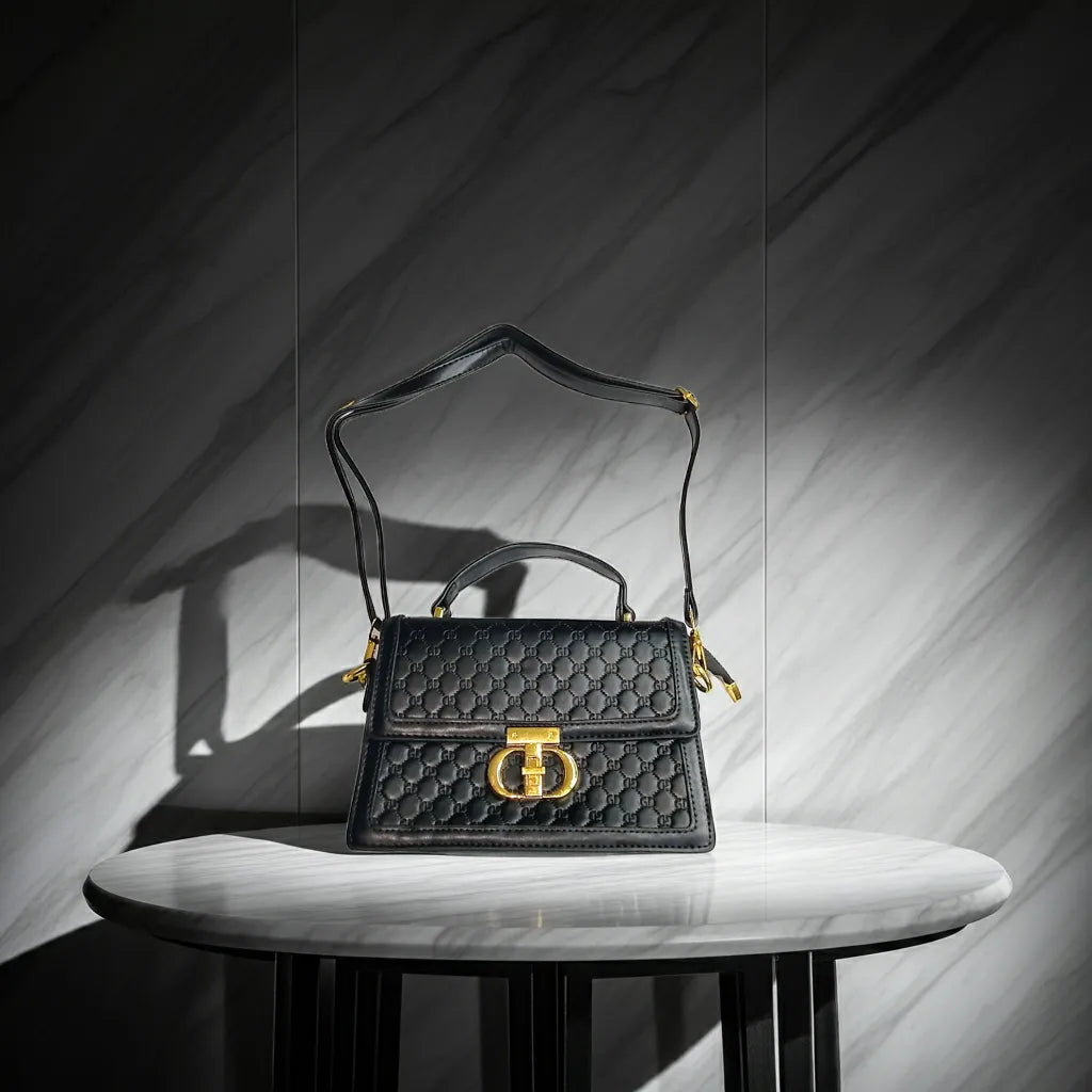 Black quilted handbag with gold accents on a marble surface against a gray marble wall.