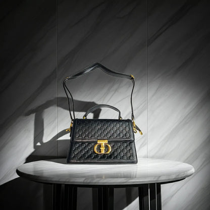 Black quilted handbag with gold accents on a marble surface against a gray marble wall.