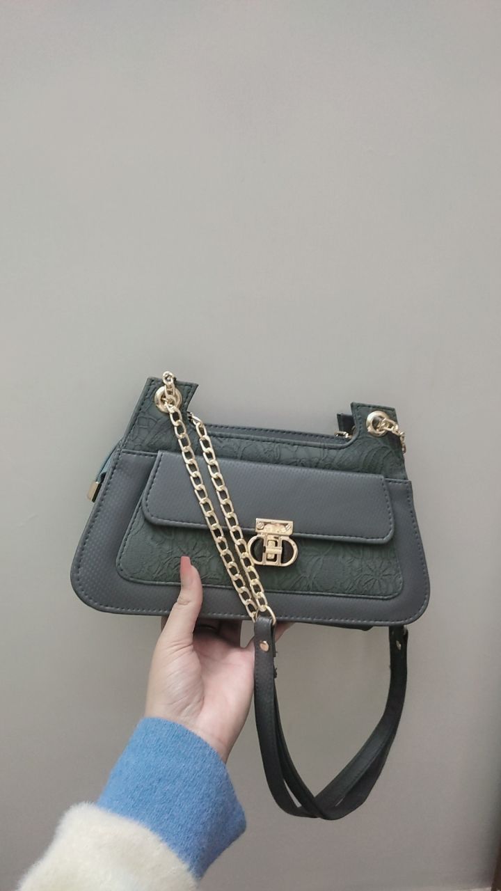 Gray handbag with a gold chain held by a person against a plain background