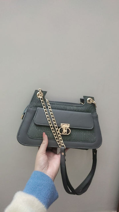 Gray handbag with a gold chain held by a person against a plain background