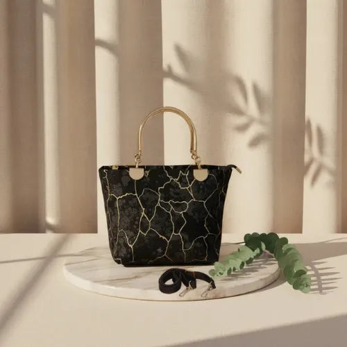 Black marble-patterned handbag with gold handle on a white surface with a neutral background