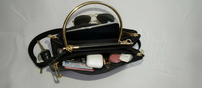 Black handbag with gold accents containing sunglasses, a phone, and other items on a white background
