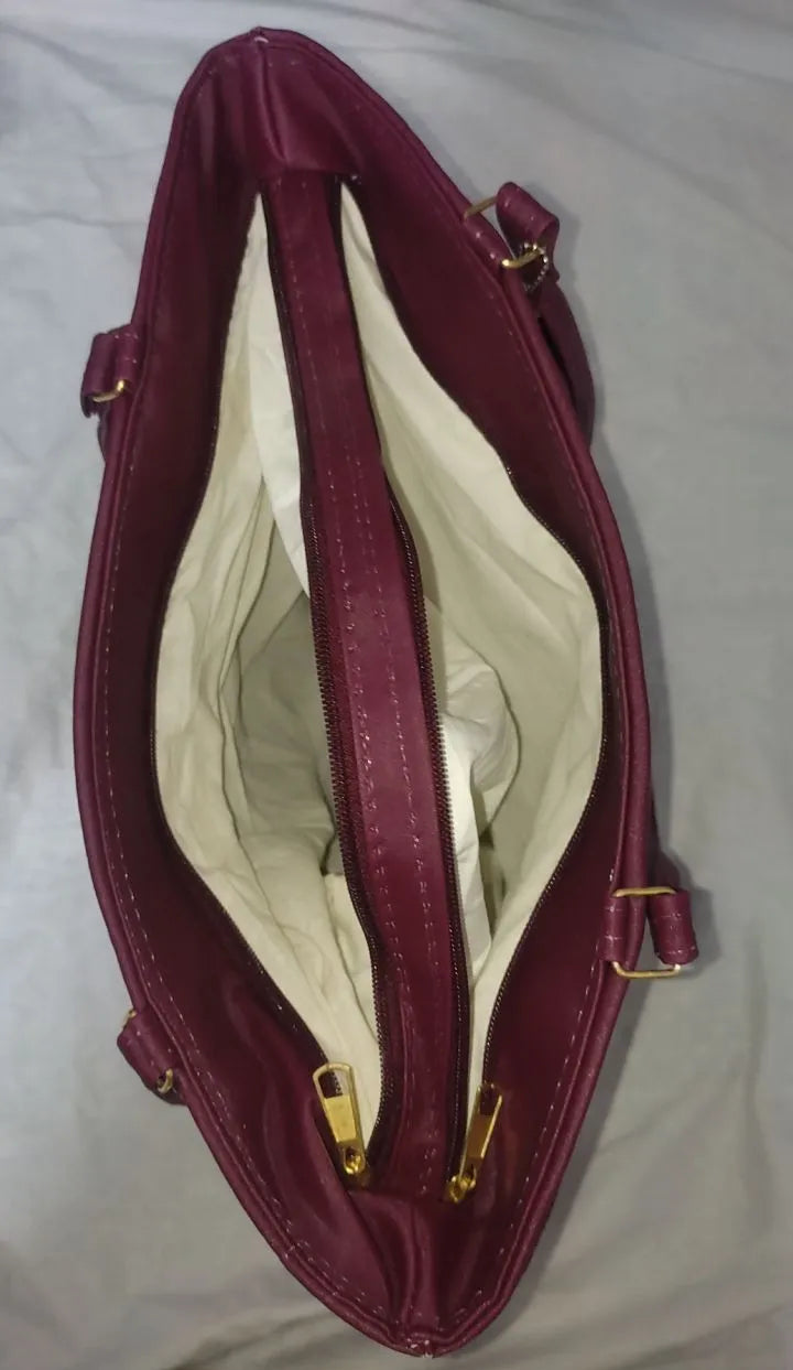 Open maroon handbag with gold zippers on a light gray background