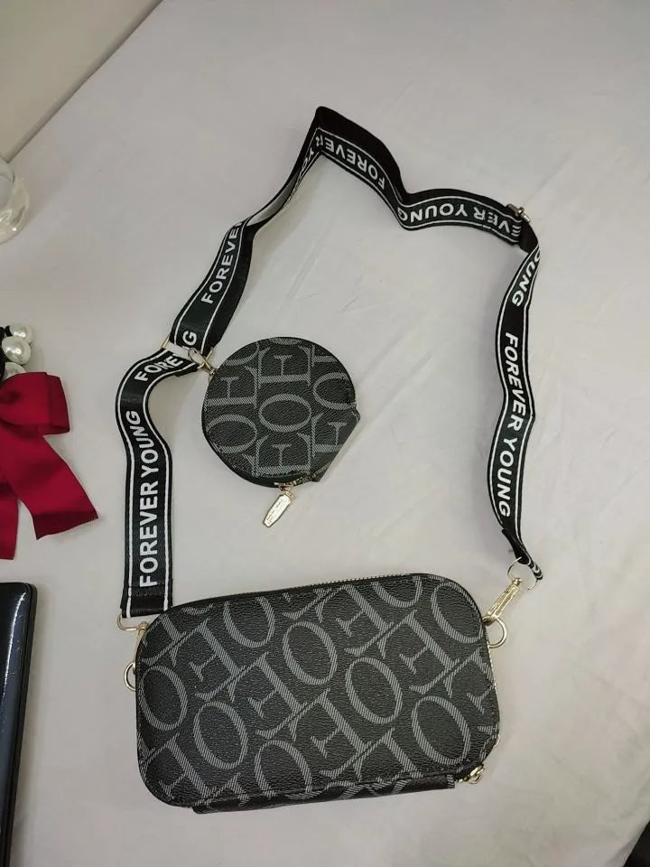 Black patterned crossbody bag with 'Forever Young' strap on a white surface