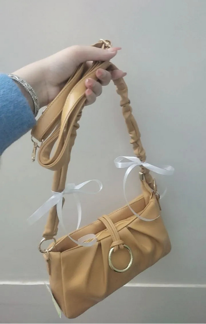 Beige handbag with a strap held by a hand against a plain background