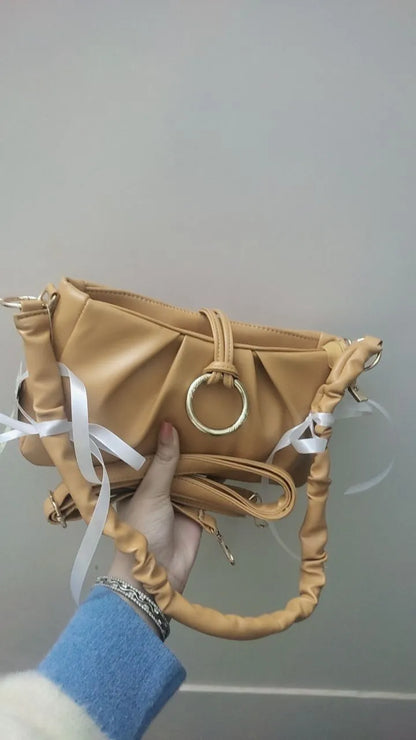 Tan leather handbag with a circular handle held by a person against a gray background