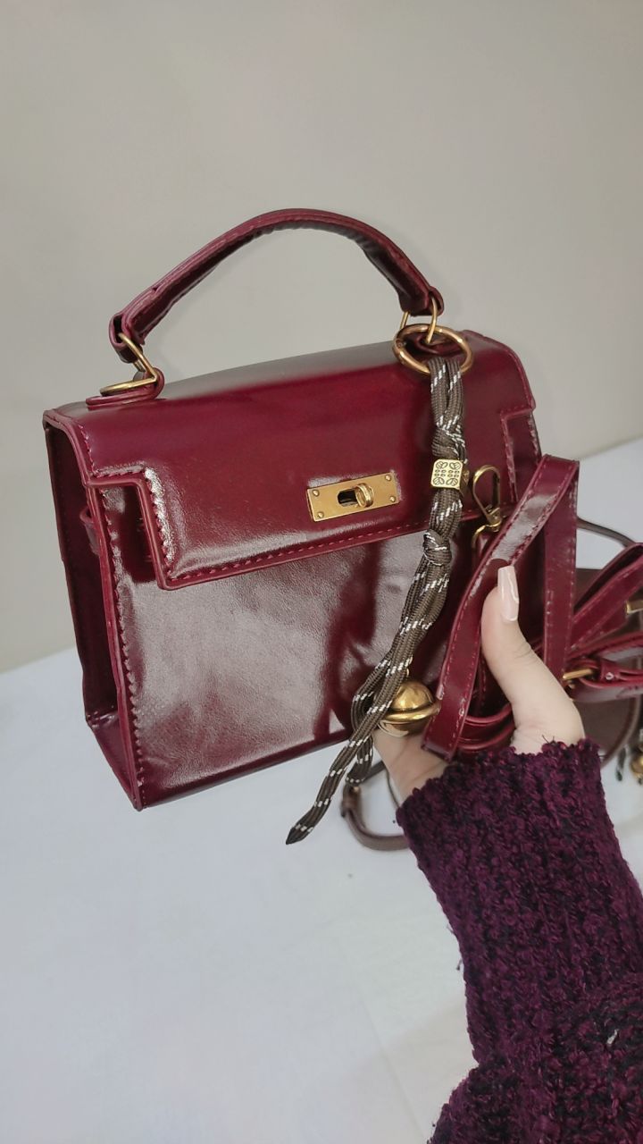 Maroon handbag with gold accents held by a person wearing a matching sweater.