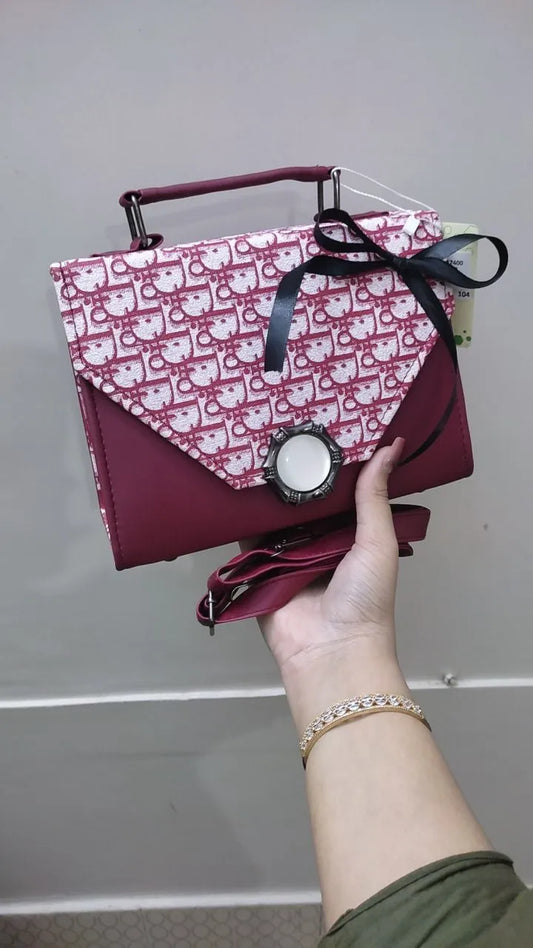 Maroon handbag with pink pattern held by a hand against a plain background