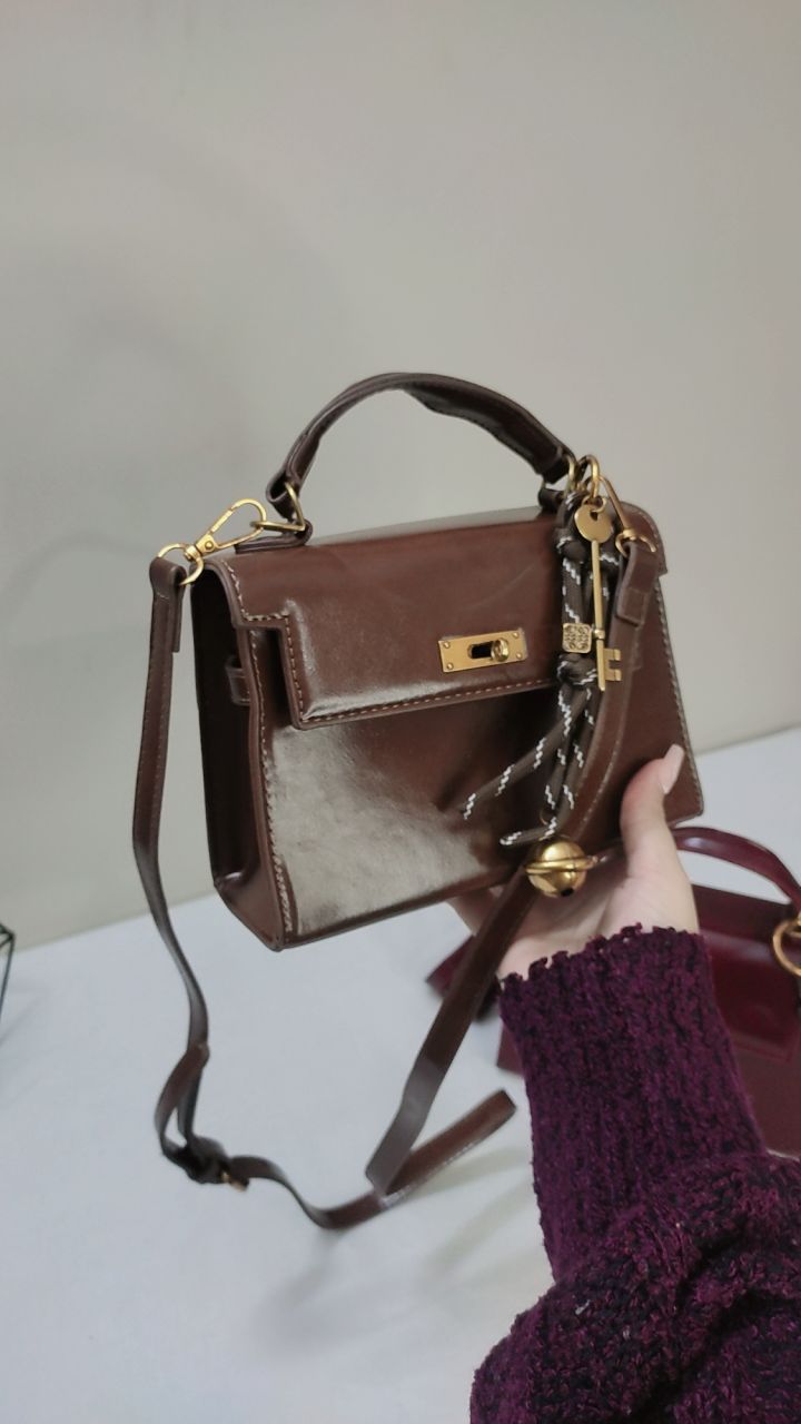 Brown handbag with gold accents held by a person wearing a purple sweater.