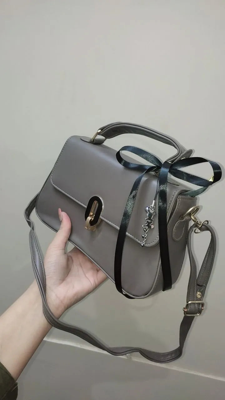 Gray handbag with a black ribbon held by a hand against a plain background