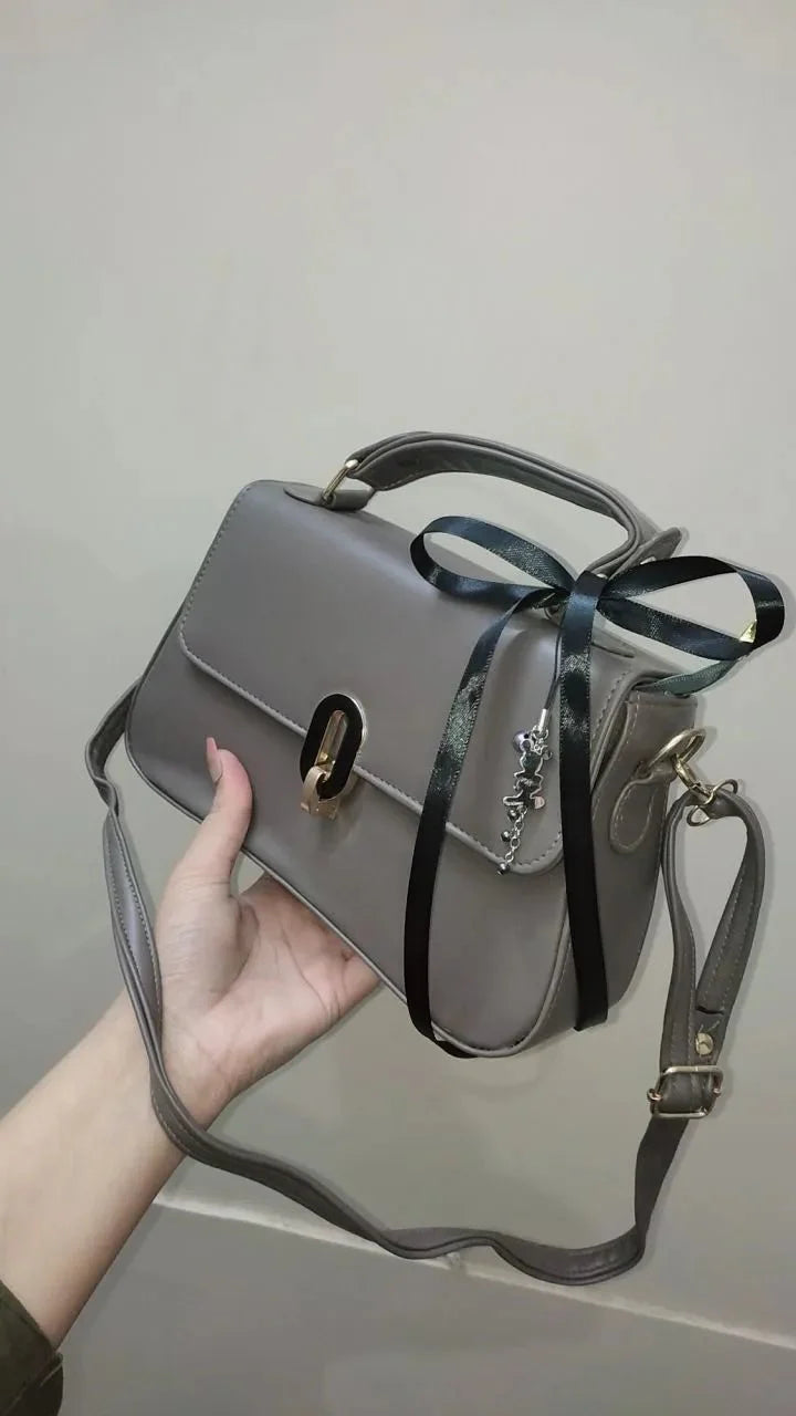 Gray handbag with a black ribbon held by a hand against a plain background