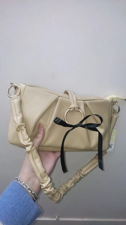 Beige handbag with a black ribbon held by a person against a plain background