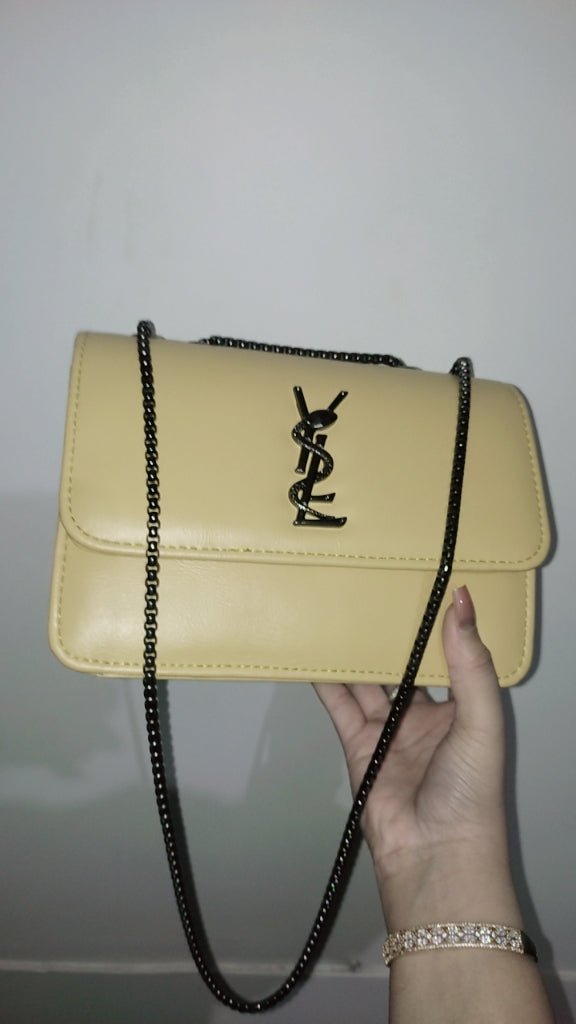 Beige handbag with a chain strap held by a hand against a white background