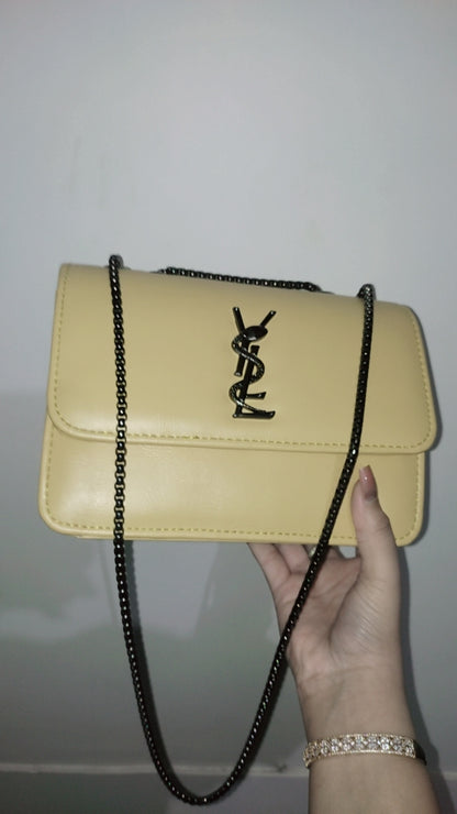 Beige handbag with a chain strap held by a hand against a white background