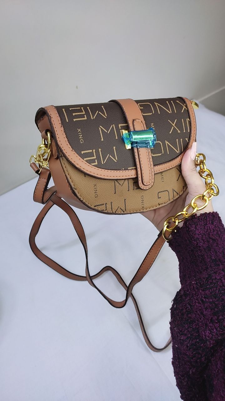 Brown handbag with gold accents held open by a hand, with a visible brand tag.