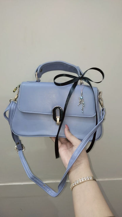 Light blue handbag with a black ribbon held by a hand against a plain background