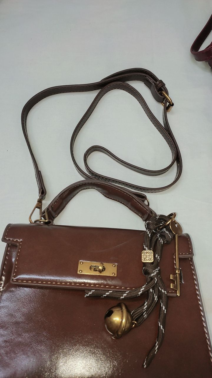 Brown leather handbag with a strap and decorative elements on a white background