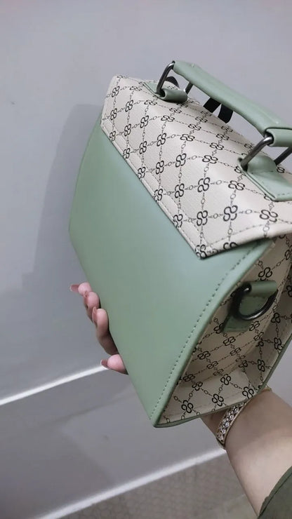 Green handbag with a patterned flap held by a hand against a neutral background