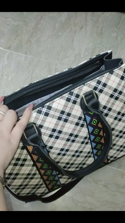 Bag with a colorful strap held by a hand on a checkered floor.