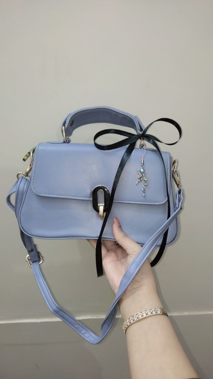 Light blue handbag with a black ribbon held by a hand against a plain background