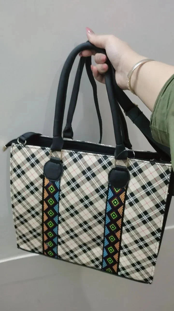 Handbag with plaid pattern and colorful strap held by a person against a neutral background