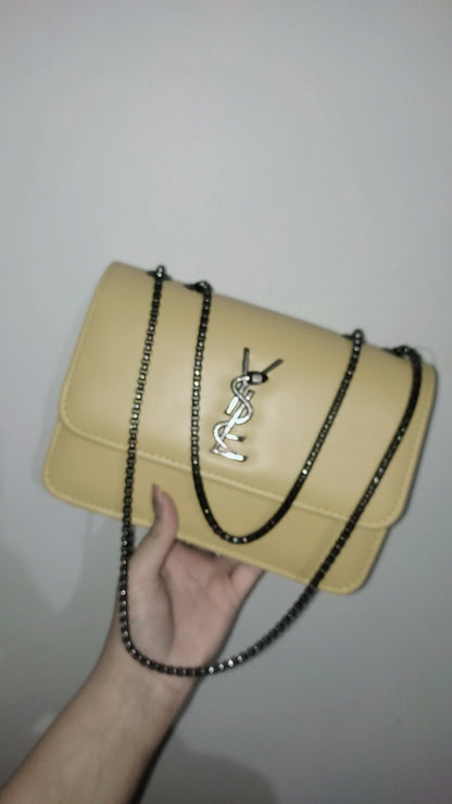 Beige handbag with a chain strap held by a hand against a plain background