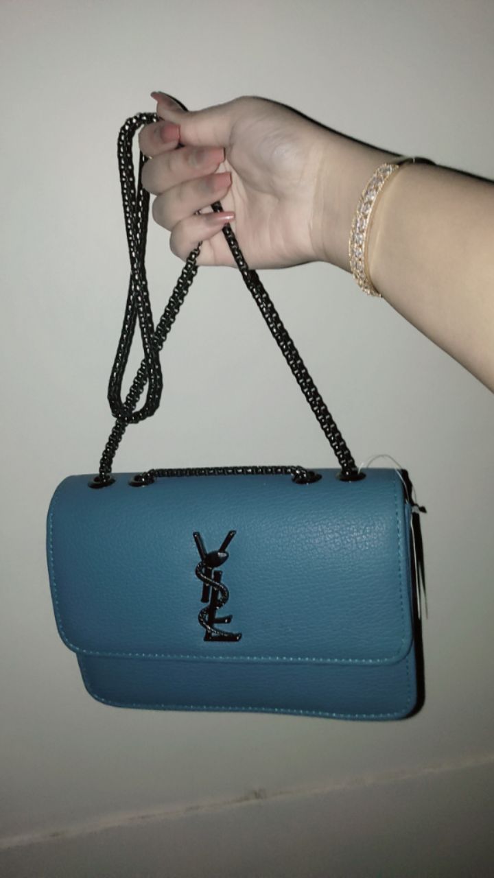 Blue handbag with a black logo held by a hand against a plain background