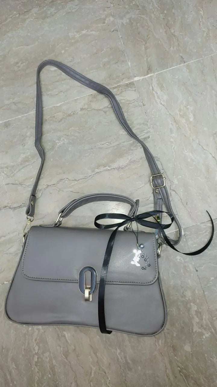 Gray handbag with a black strap on a light gray tiled floor