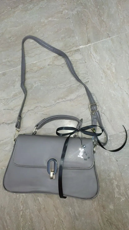 Gray handbag with a black strap on a light gray tiled floor