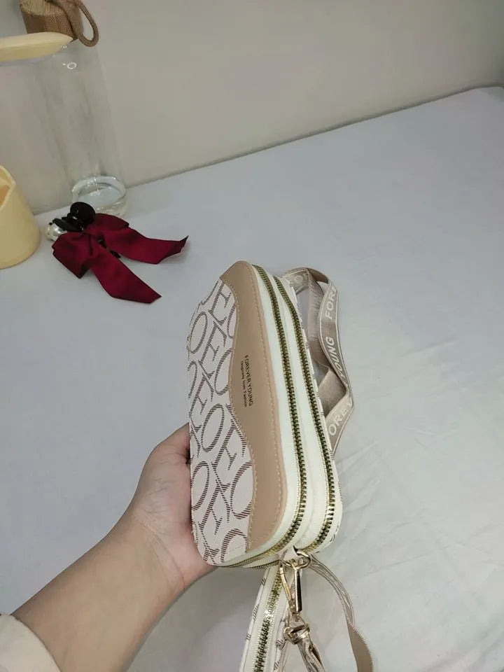 Beige handbag with brand logo held by a hand on a light-colored surface.