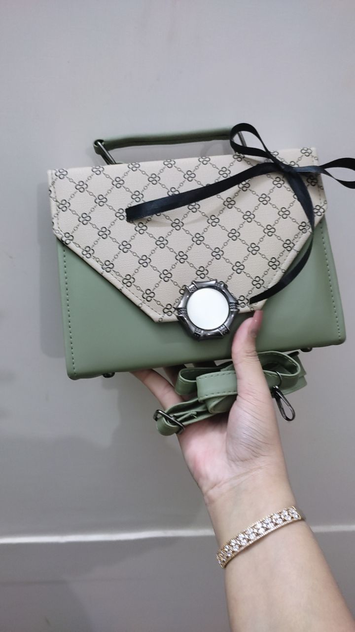 Green handbag with patterned flap held by a hand against a neutral background