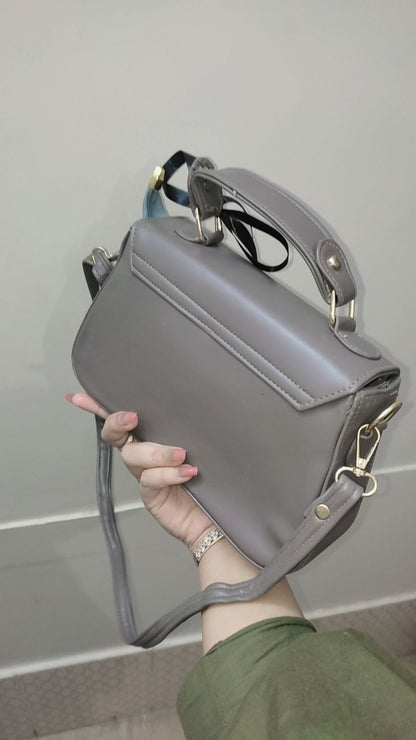 Gray handbag held by a person against a neutral background
