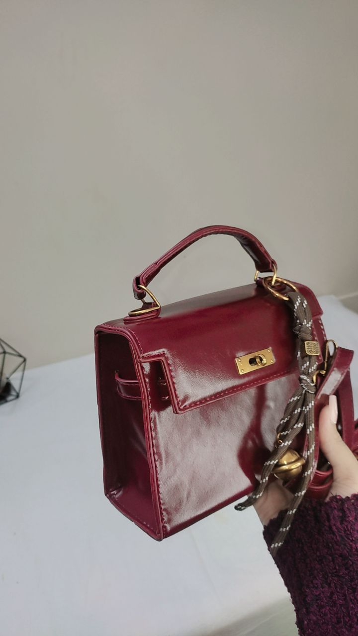 Red handbag with gold accents held by a person against a neutral background