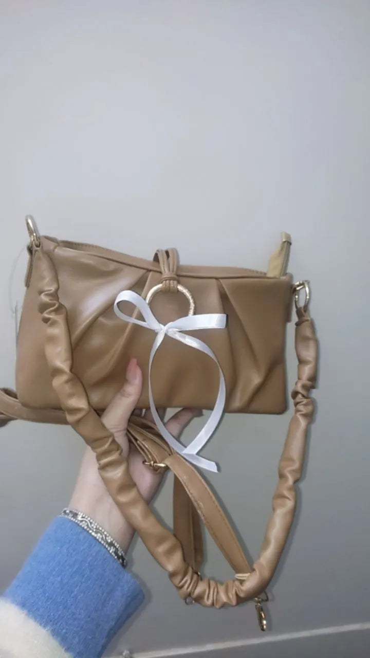 Brown handbag with a white ribbon held by a person wearing a blue sleeve.