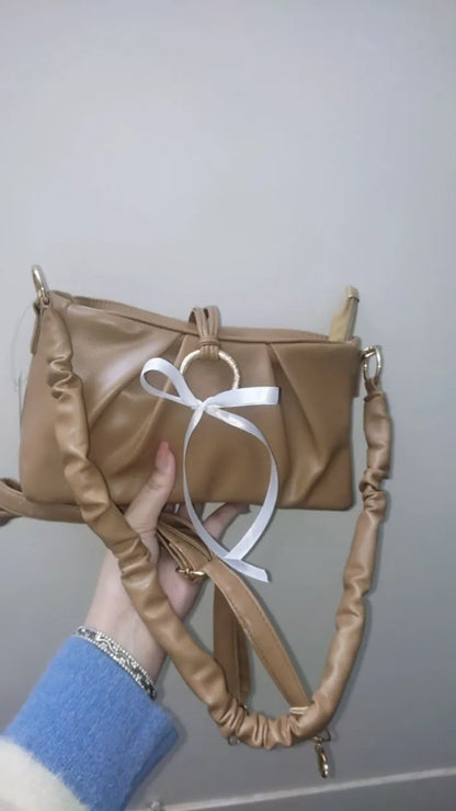 Brown handbag with a white ribbon held by a person wearing a blue sleeve.