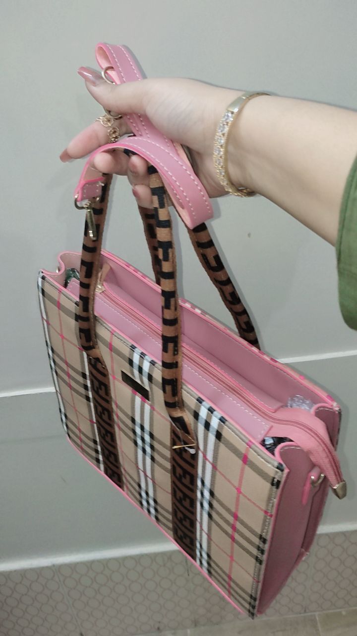 Pink handbag with plaid pattern held by a person against a neutral background