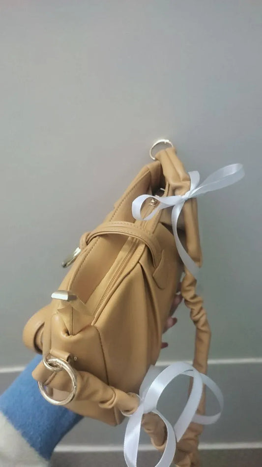 Tan leather handbag with white ribbons on a gray background