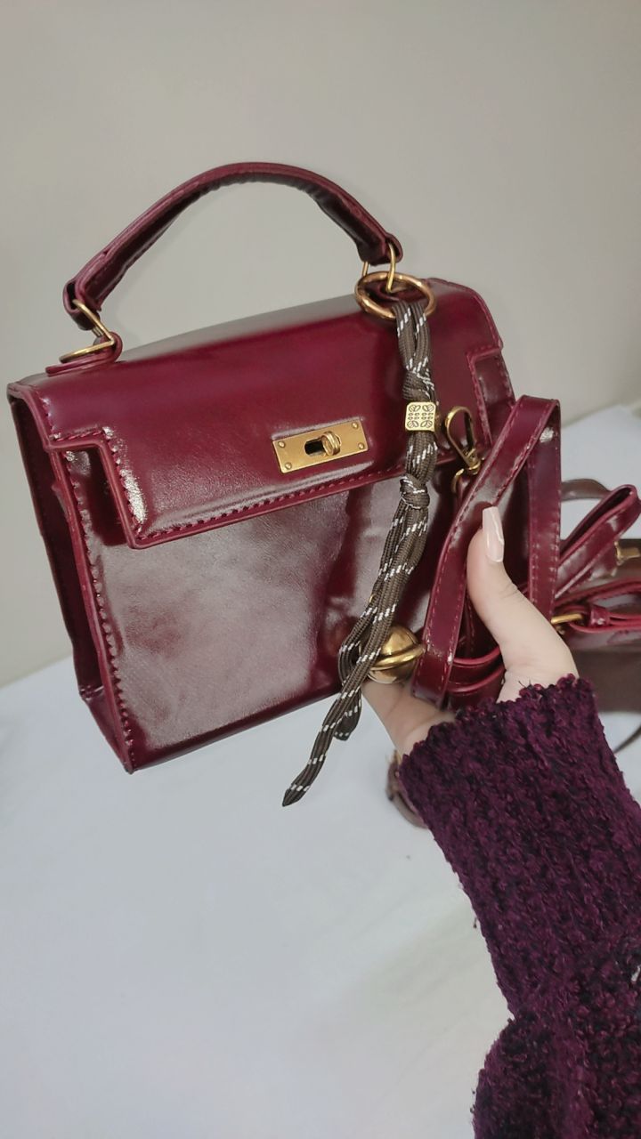 Burgundy handbag with gold accents held by a person wearing a matching burgundy sweater.