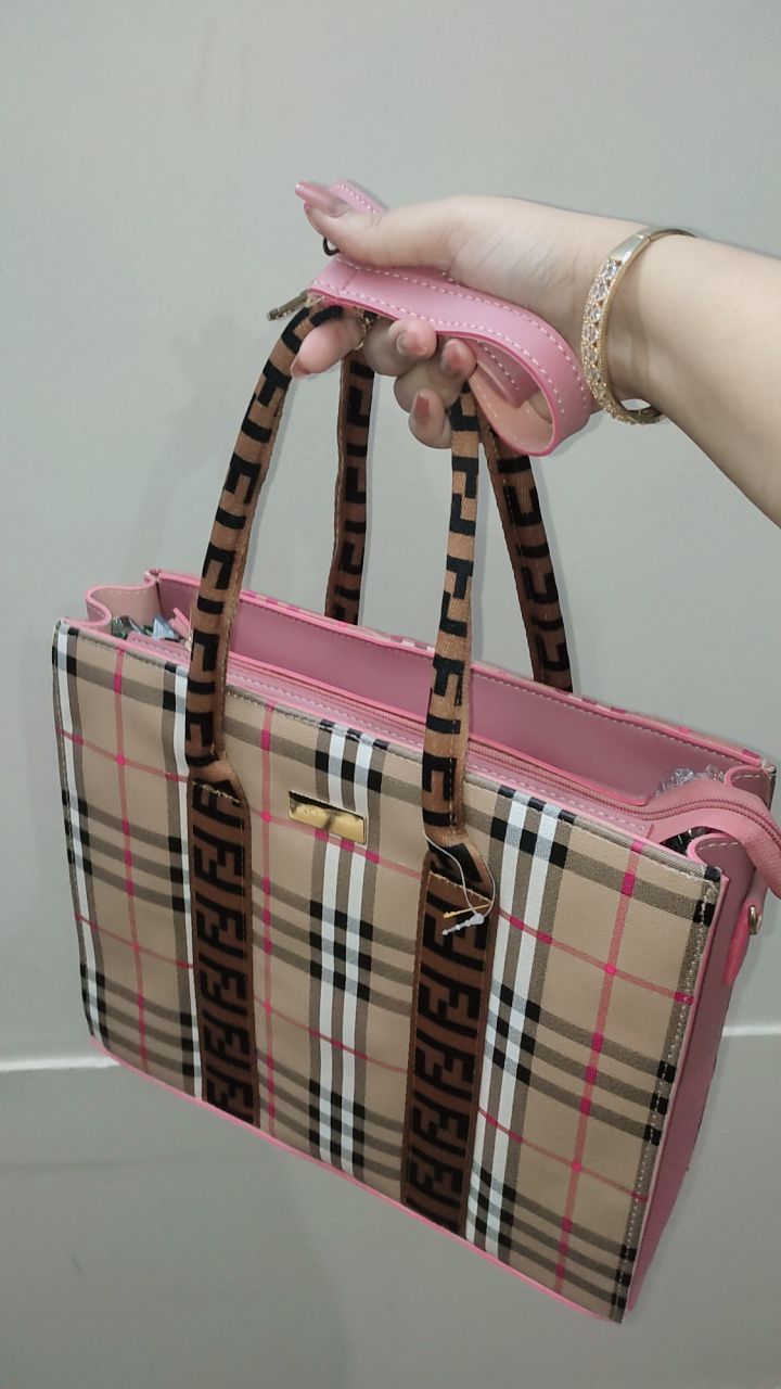 Pink and plaid handbag held by a person against a plain background