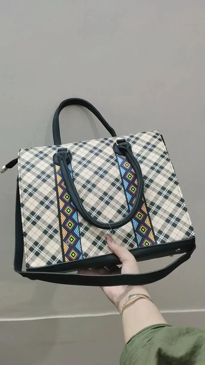 Hand holding a plaid bag with decorative straps against a gray background