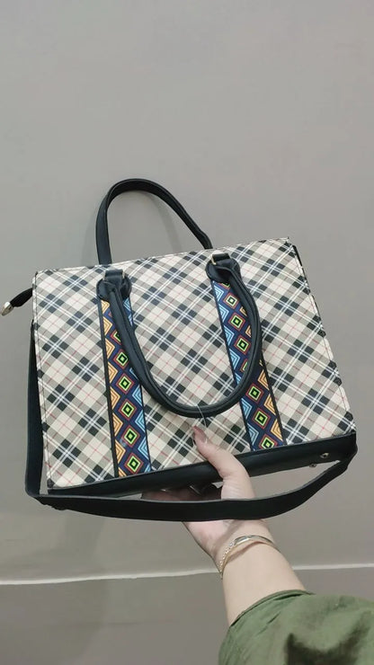 Hand holding a plaid bag with decorative straps against a gray background