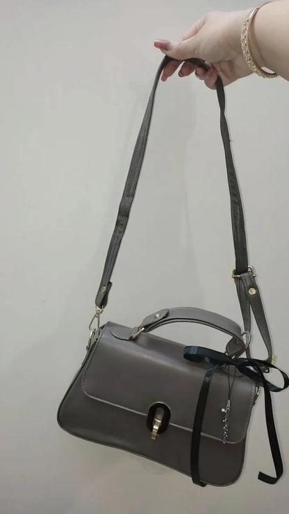Gray handbag with a black strap held by a hand against a plain background